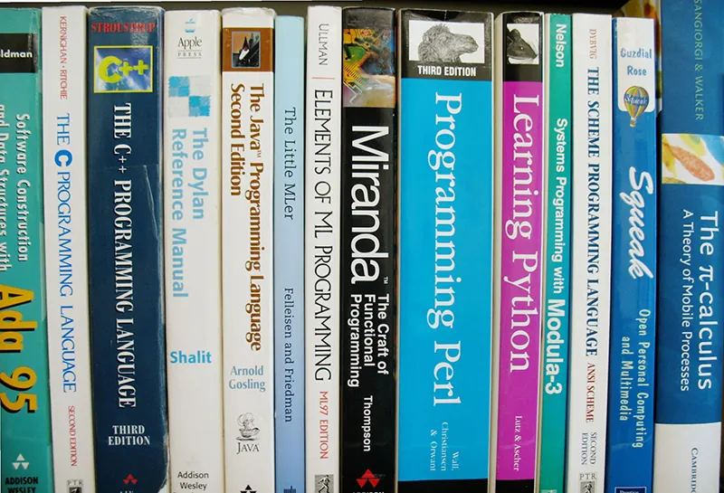 A book shelf holds a number of textbooks, mostly related to computer programming.