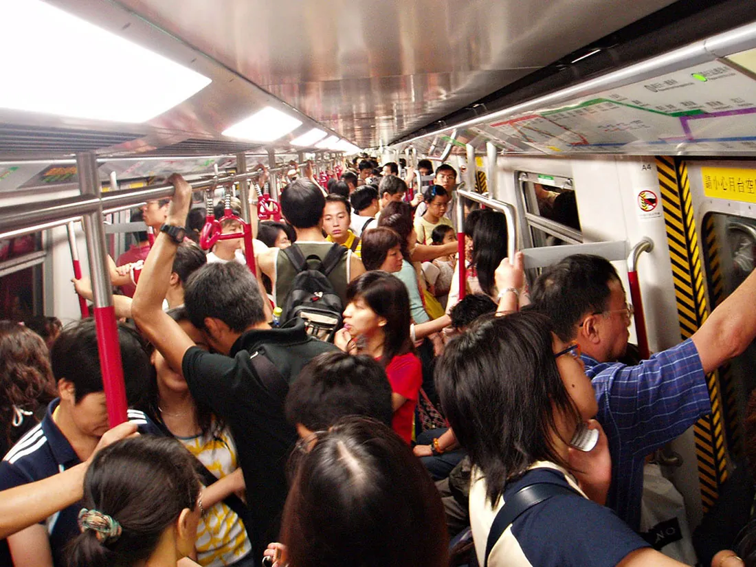 A view of the inside of a crowded commuter train. People lean on walls and hold on to railings.