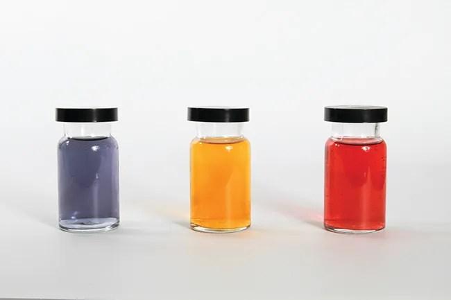 Esta figura exhibe tres recipientes llenos de líquidos de diferentes colores. El primero parece ser púrpura, el segundo, naranja, y el tercero rojo.