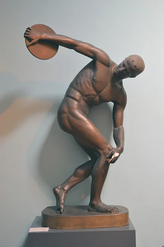 Statue of an athletic man extending his arm behind him to throw the discus in his hand.