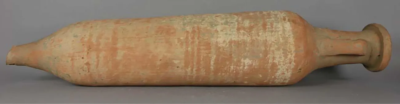 An earthenware object is shown on a gray background. It is long, round, and faded gray, white, and rust colored. The left end has a broken point, the middle is thicker, and the right side is thinner with a rounded, circular end and a handle visible on the front.