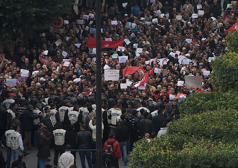 A large crowd fills the street. Many people hold signs and placards.