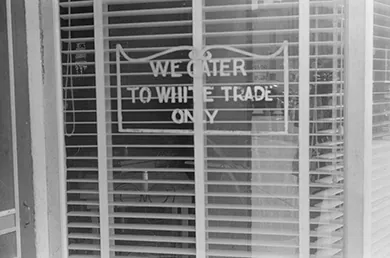 A photograph shows a shop window bearing a sign that reads “We cater to White trade only.”