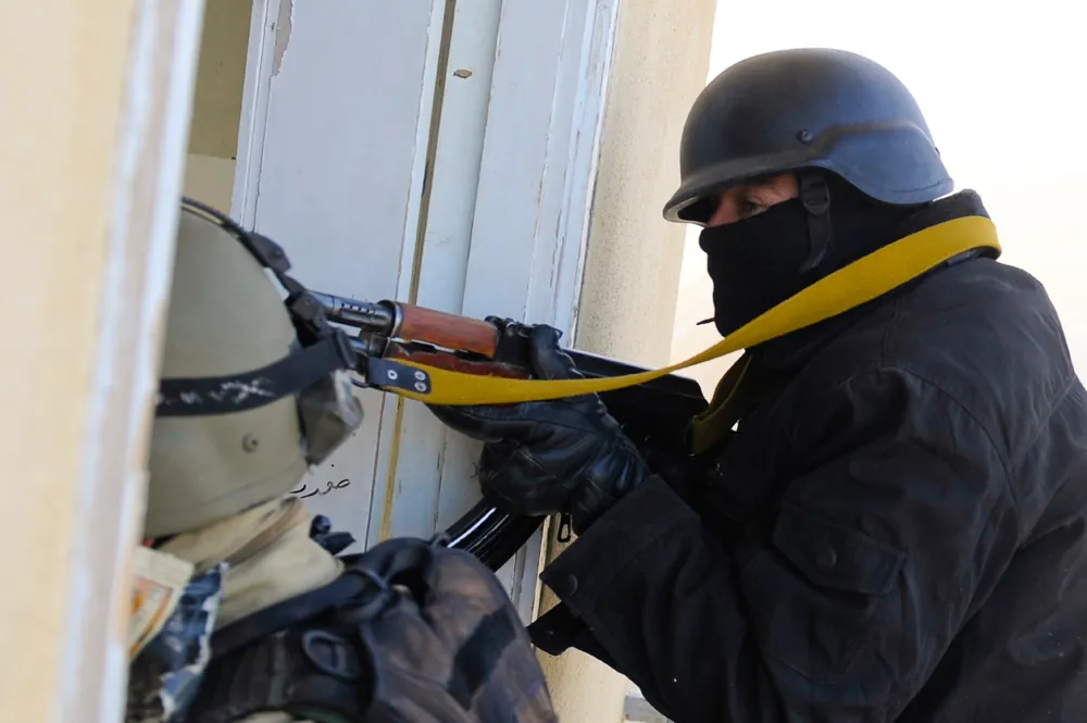 An armed and armored police officer is shown in a doorway with his gun.
