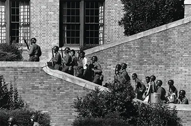 A photograph shows uniformed soldiers holding rifles as they escort the Little Rock Nine up the steps of Central High School.