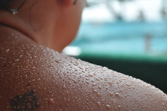 Se muestra el hombro y el cuello de una persona y su piel está cubierta de gotas de líquido.