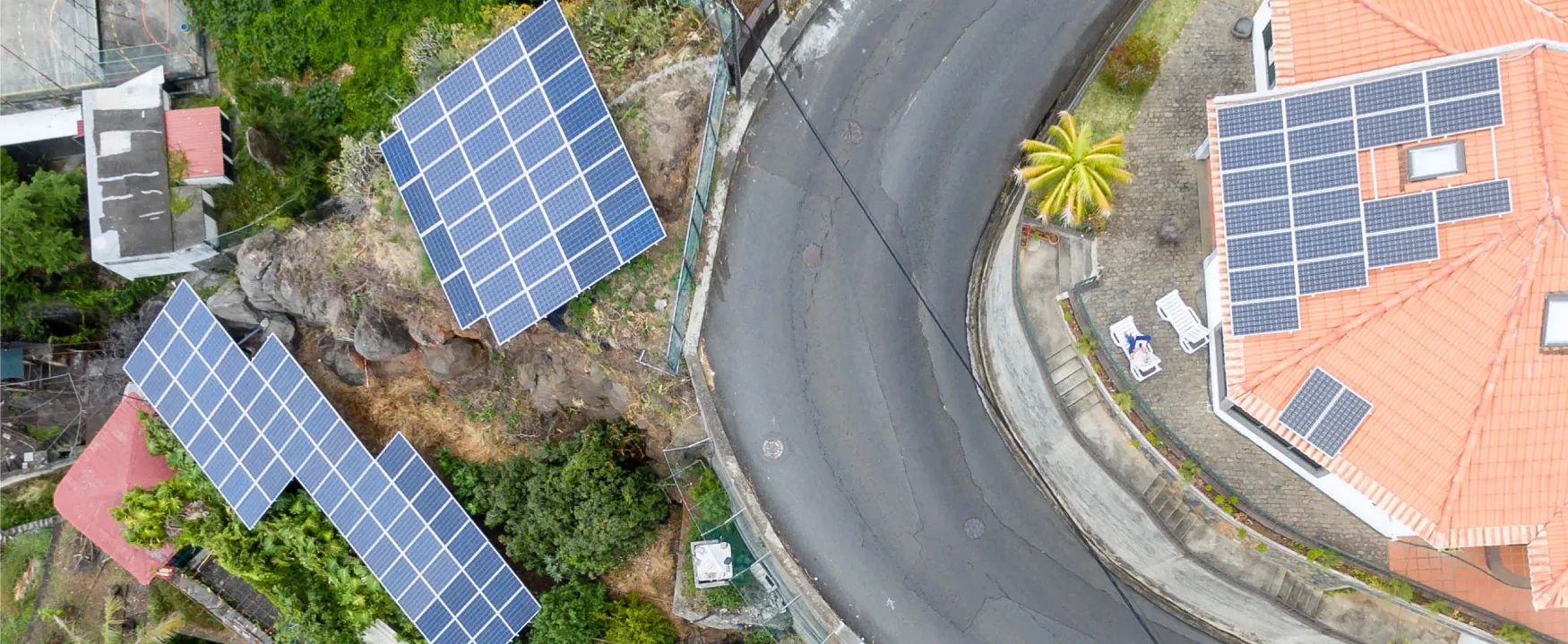 An aerial photograph shows houses on a tropical hillside with solar panels on their roofs.