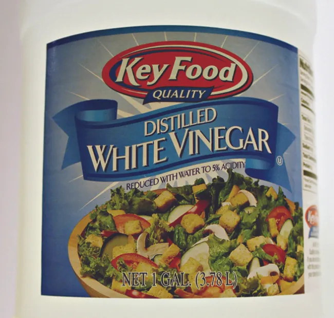 Una imagen muestra la etiqueta de una botella de vinagre blanco destilado. En la etiqueta se indica que el contenido se ha reducido con agua a un 5% de acidez.