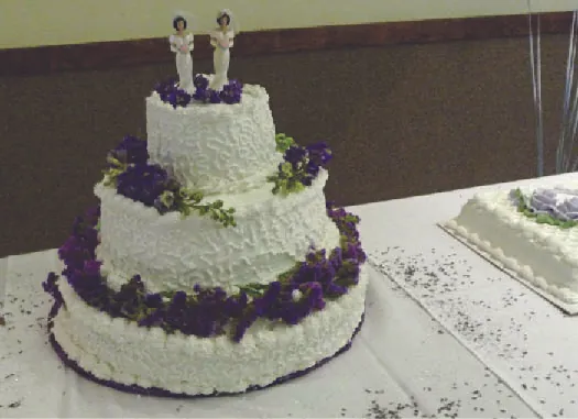 A photo of a cake with three tiers. Two human figurines appear on the top tier.