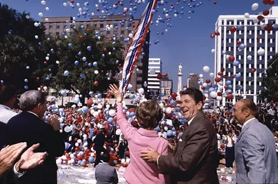 A photograph shows Ronald and Nancy Reagan on the campaign trail. They stand amidst a cheering crowd, surrounded by red, white, and blue balloons. Nancy Reagan waves to the crowd; Ronald Reagan smiles and places a hand on her back.