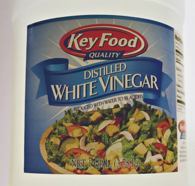 Se muestra la etiqueta de un contenedor. La etiqueta tiene el dibujo de una ensalada con las palabras “Vinagre blanco destilado” y “Reducido con agua hasta el 5 % de acidez".