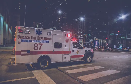 An image of a truck with flashing lights driving through an intersection. The side of the truck reads “Chicago Fire Department Emergency Medical Services”.