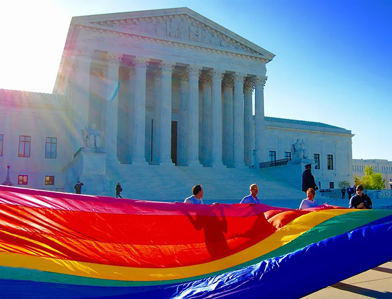 People hold a very large rainbow flag in front of the United States Supreme Court.