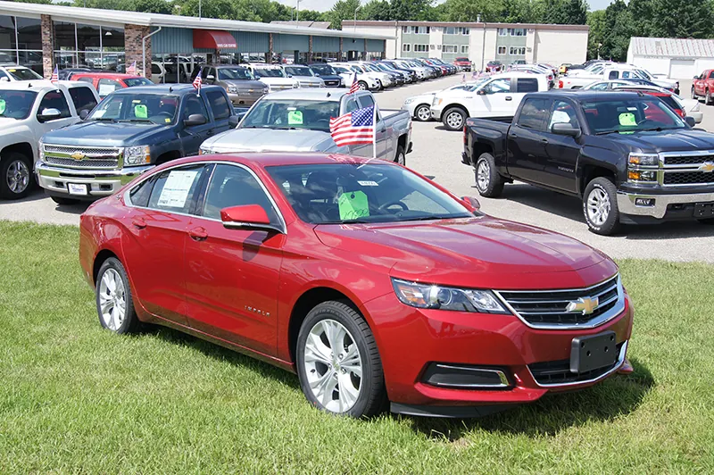 A Chevrolet impala car parked on a grassy patch of land. Various other cars of different make and model are parked behind in what seems like a parking lot.