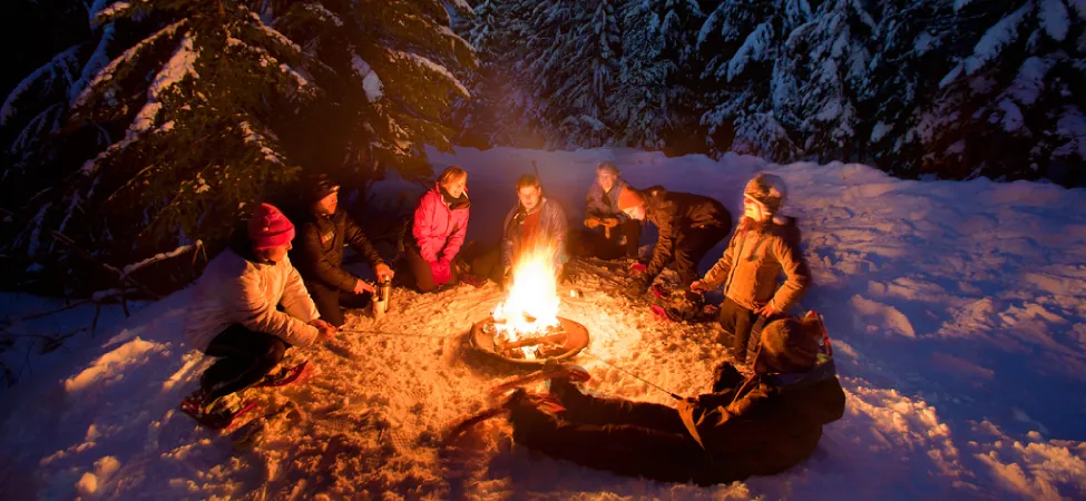 Fotografía de personas sentadas alrededor de una hoguera en la nieve.