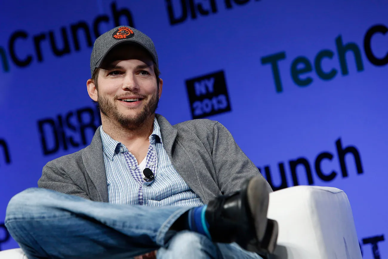 A photograph shows Ashton Kutcher sitting in front of a digital screen that reads Tech Crunch, N Y 2013.