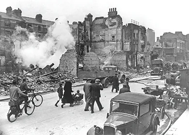 A photograph shows a destroyed London street in which most of the buildings have been reduced to rubble; citizens stroll past with bicycles and a child in a pram