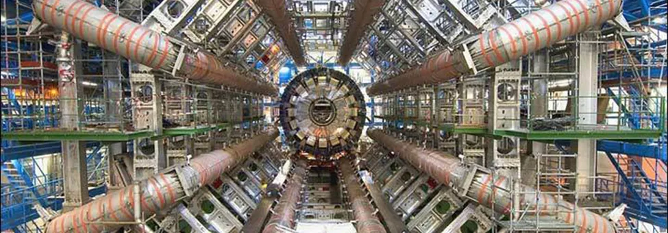 The photograph shows a series of tubes and structural elements that make up the Large Hadron Collider. The five staircases on the sides of the collider show the very large size of the experimental device.