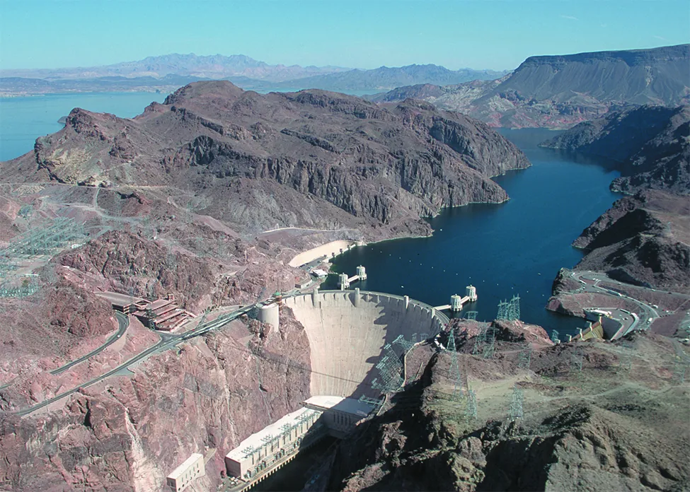 This is a picture of the Hoover Dam. The picture has the dam in the background and flowing water in the foreground below the dam.