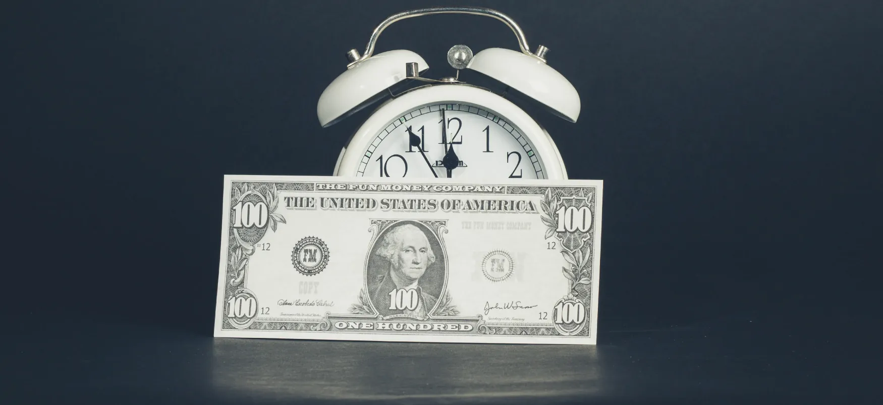 A $100 bill leans against an alarm clock.