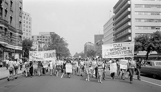 A photograph shows a protest march of women on a city street. Participants hold signs with messages such as “Women Demand Equality;” “I’m a Second Class Citizen;” and “GWU Women’s Liberation. Students Employees Faculty Wives Neighbors.”