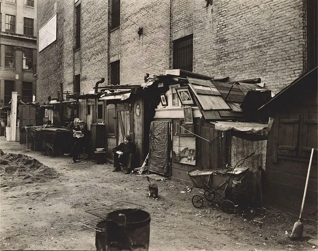 A photograph shows a row of urban shanties, with several of their inhabitants sitting outside.
