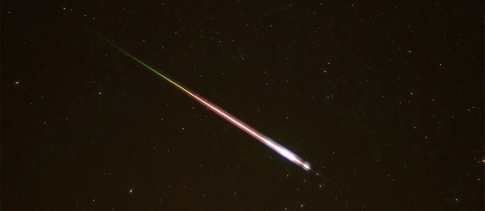 This is a photo taken of the night sky. A meteor and its tail are shown entering the earth's atmosphere.