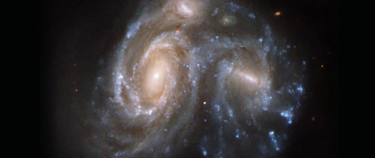 Hubble Space Telescope image of two interacting galaxies. A larger spiral galaxy with a circular nucleus is on the left, in contact with a smaller barred-spiral galaxy on the right.