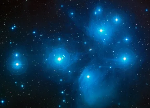 The Pleiades. The light from the bright, blue stars of this cluster reflects off of the nearby dust clouds, giving the appearance of streetlamps on a foggy night.