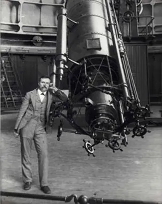 Photograph of Edward Emerson Barnard leaning against a large telescope.