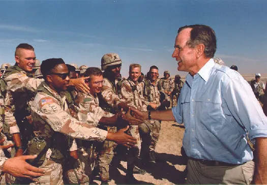 George H. W. Bush shaking hands with U.S. troops outdoors.