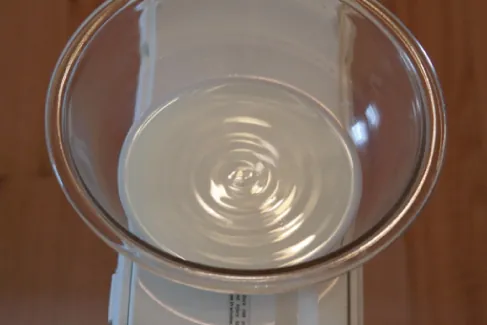 Fotografia przedstawia fale na powierzchni miski z mlekiem, umieszczonej na obudowie wiatraka.