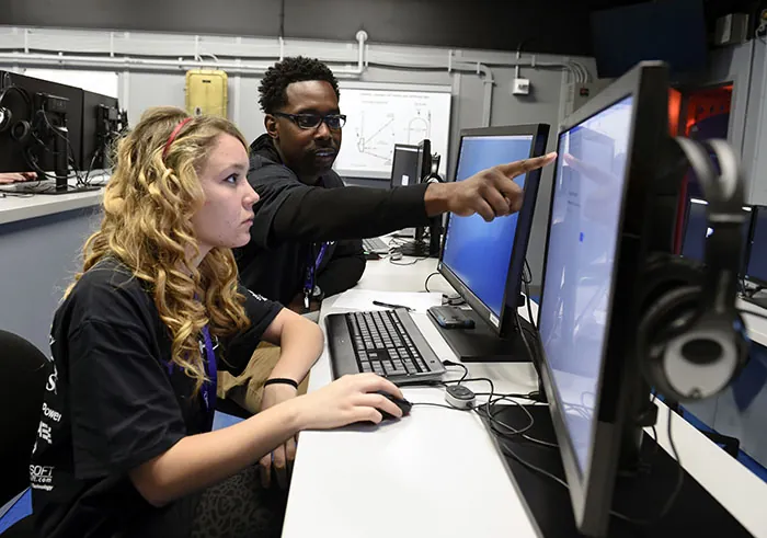 An instructor helps a student by pointing something out on her computer screen.