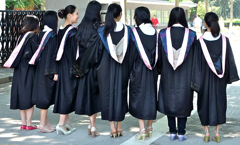 Eight girls graduating from college in their gowns, with their backs turned toward the camera