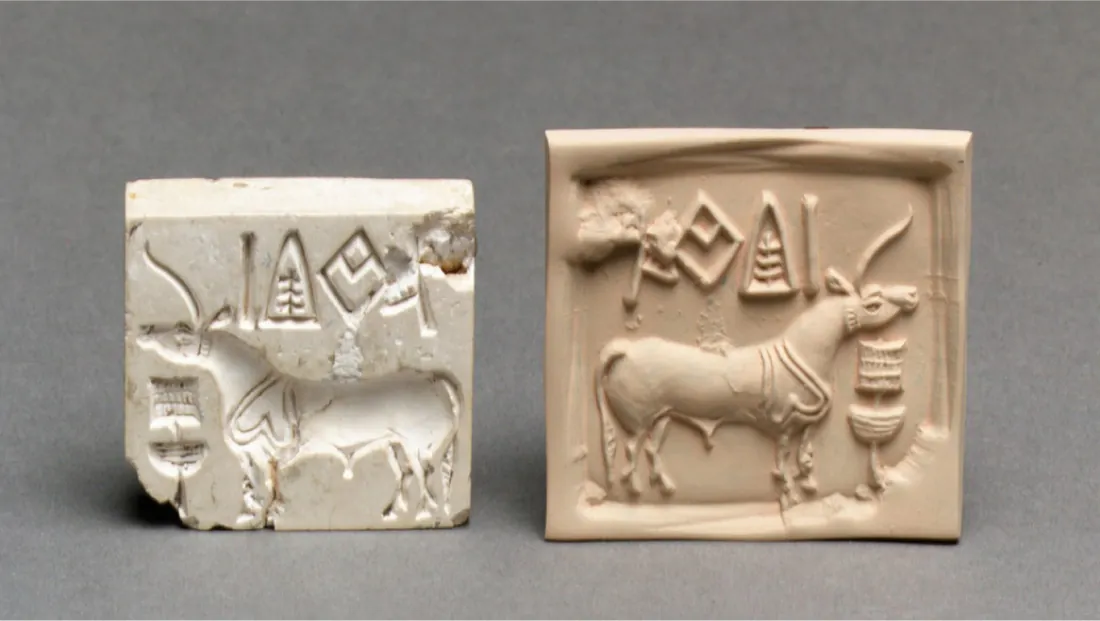 A picture of two square objects is shown on a grayish-blue background. The one on the left is white and smaller, while the one of the right is a bit bigger and a cream color. The images on the square on the right are raised from the back. They show a horse-type creature with ornamental reins around its neck and a long, pointy horn extending out its head. Above the animal are four shapes – a diamond with a v-shape inside, a triangle with lines inside, and a line, while the fourth shape is indistinguishable. Below the head of the animal is a long stick with a square at the top and a half-circle below. Both shapes have lines on them. The square at the left is an impression of the first square, showing everything backward and inside the stone as opposed to sticking out as in the other square.