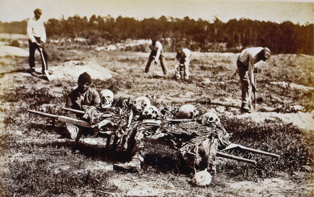 A photograph shows several African American men collecting the bones from a battleground in Virginia. In the foreground, one man prepares to carry away a pile of skulls and body parts.