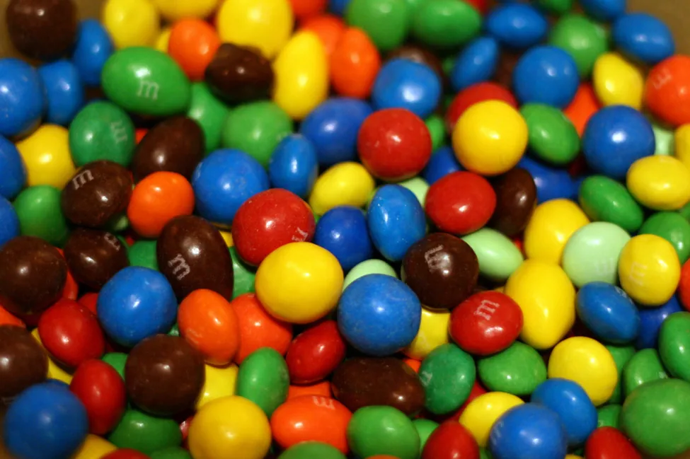Esta es una foto de M&M apilados. Los M&M son de colores rojo, azul, verde, amarillo, anaranjado y marrón.