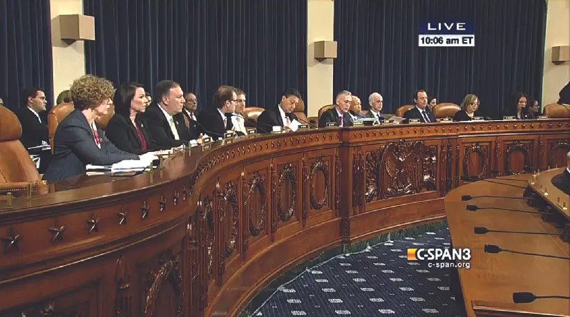 An image of several people seated behind a long wooden bench.