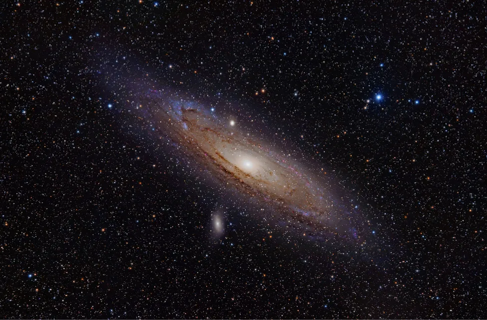 Image of the Andromeda Galaxy. This spiral galaxy is seen almost edge-on as an oval patch of light with a very bright center (nucleus), and dark bands of dust along its outer edges.