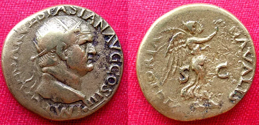 An image of two old and faded coins is shown on a pink woven background. The coin on the left is round, gold with black shading on the right side and faded letters around the perimeter. A man’s face is carved in the middle, facing to the right, with a round head, large flat nose and thick neck. The coin on the right is gold and worn. Faded letters circle parts of the perimeter and a figure with wings is shown in the middle. The figure wears a cap, extends their arm out to the right, and appears to wear long robes. The letter “S” is shown on the left and the letter “C” is shown on the right.