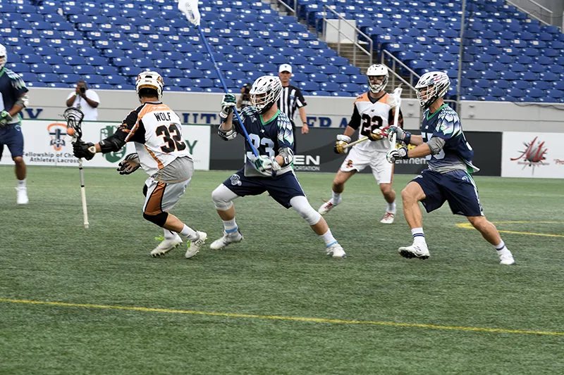 Lacrosse players wearing professional uniforms and helmets in the middle of a game.