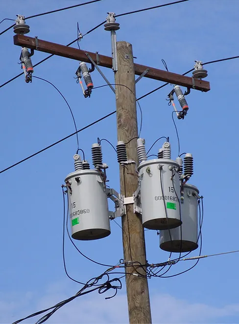 Fotografía de transformadores en un poste eléctrico. Hay tres transformadores, cada uno encerrado en un contenedor cilíndrico.