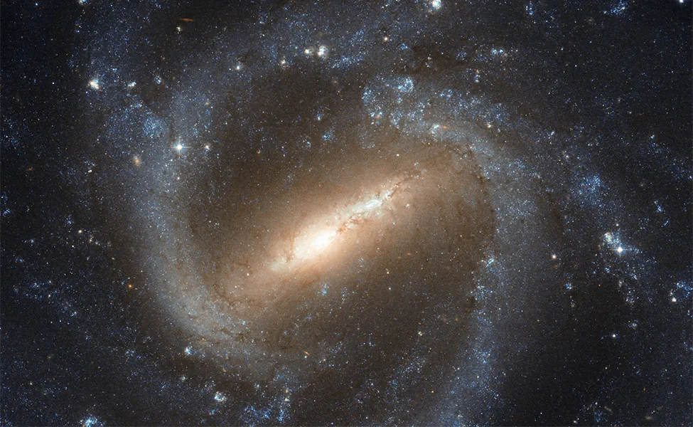 Image of a Barred-Spiral Galaxy. Just below center is the elongated central bar tilted about 45-degrees from the bottom of the frame. At each end of the bar begin the spiral arms, twisting clockwise around the central bar and encircling the whole galaxy.