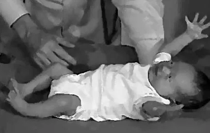 Photo of infant laying down with arms and legs sticking straight out and up.