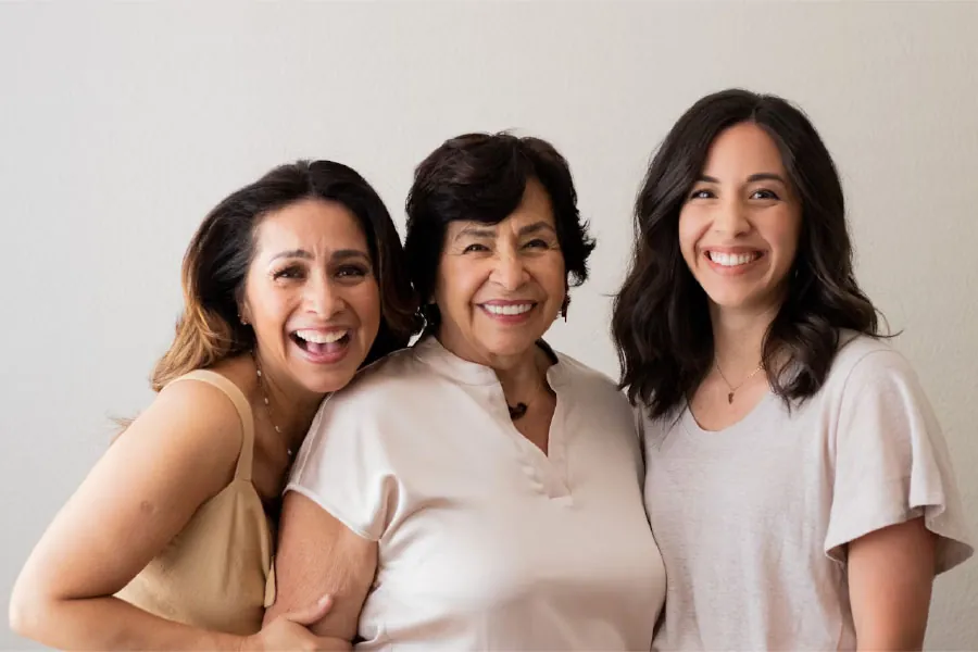 Photo of a grandparent, parent, and young adult standing together and smiling.