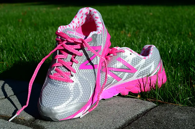 A pair of New Balance running shoes are displayed in a grassy area.