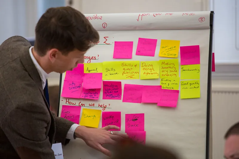 A person pastes yellow and pink sticky notes on white chart paper as they brainstorm potential topics for an advocacy project.