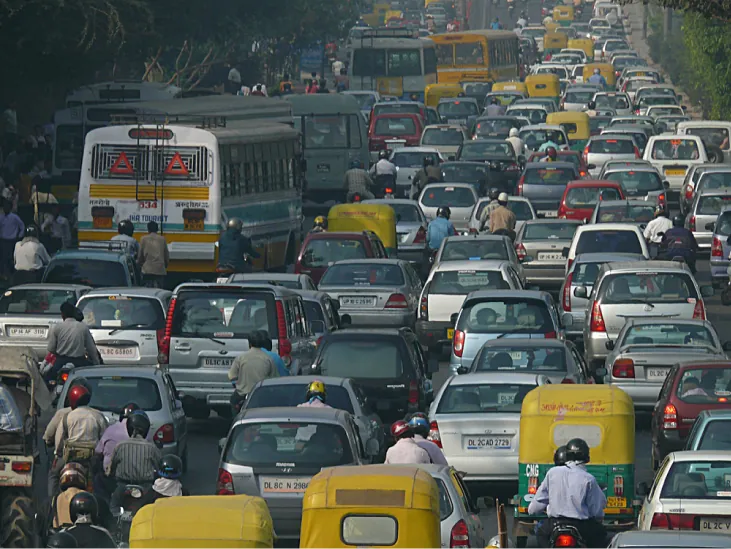 Zdjęcie przedstawia zakorkowaną przez samochody i motocykle drogę w Delhi.