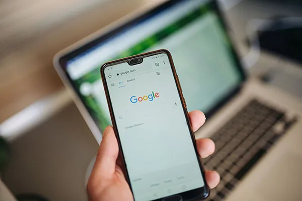 A person is looking at a phone. A laptop is in the background.