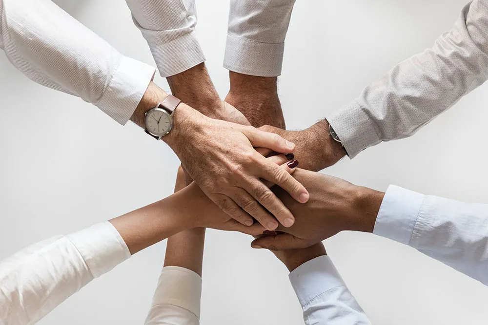 A photo shows six hands of different people joining to indicate an agreement.